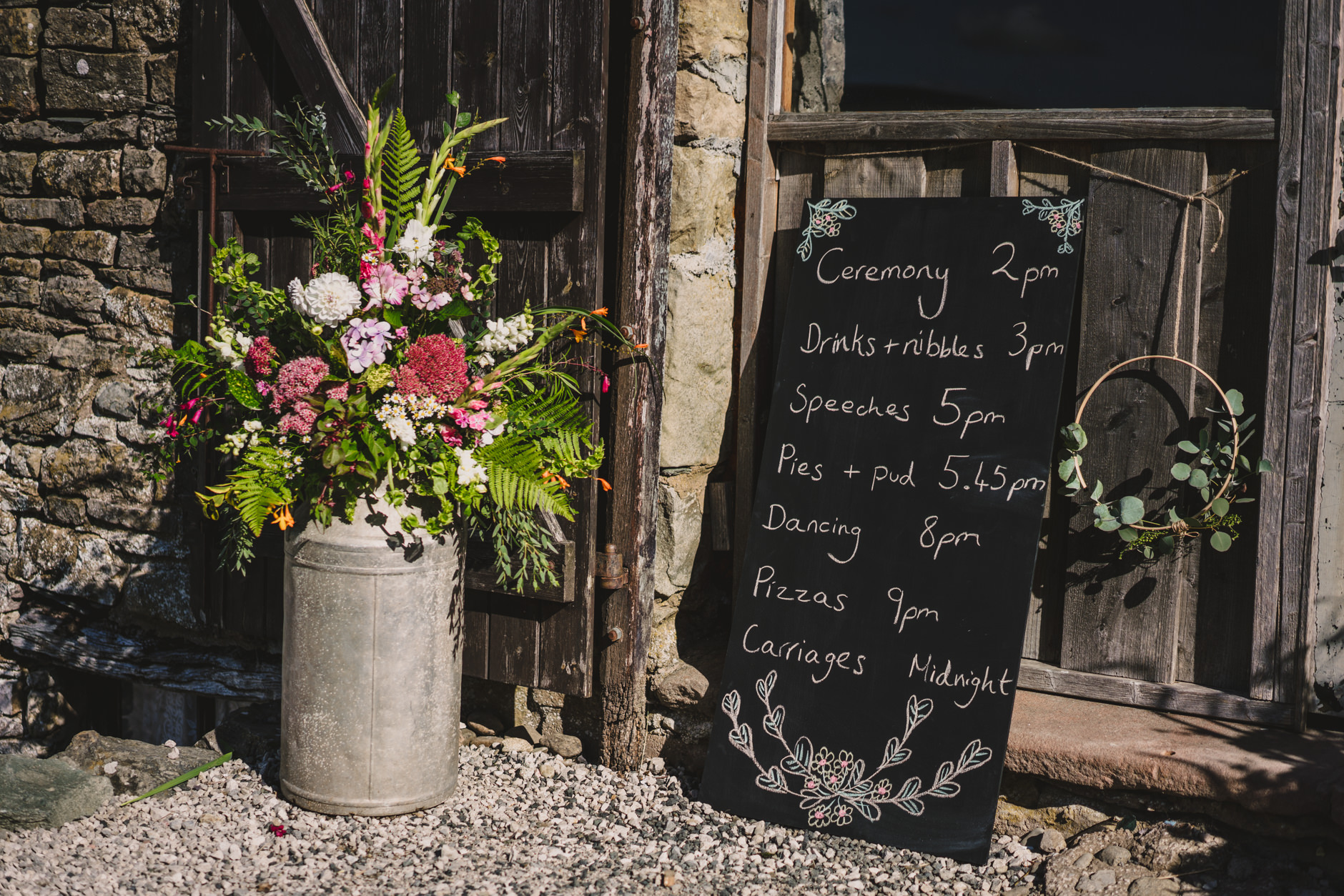 DIY wedding timeline blackboard and milk churn full of garden flowers