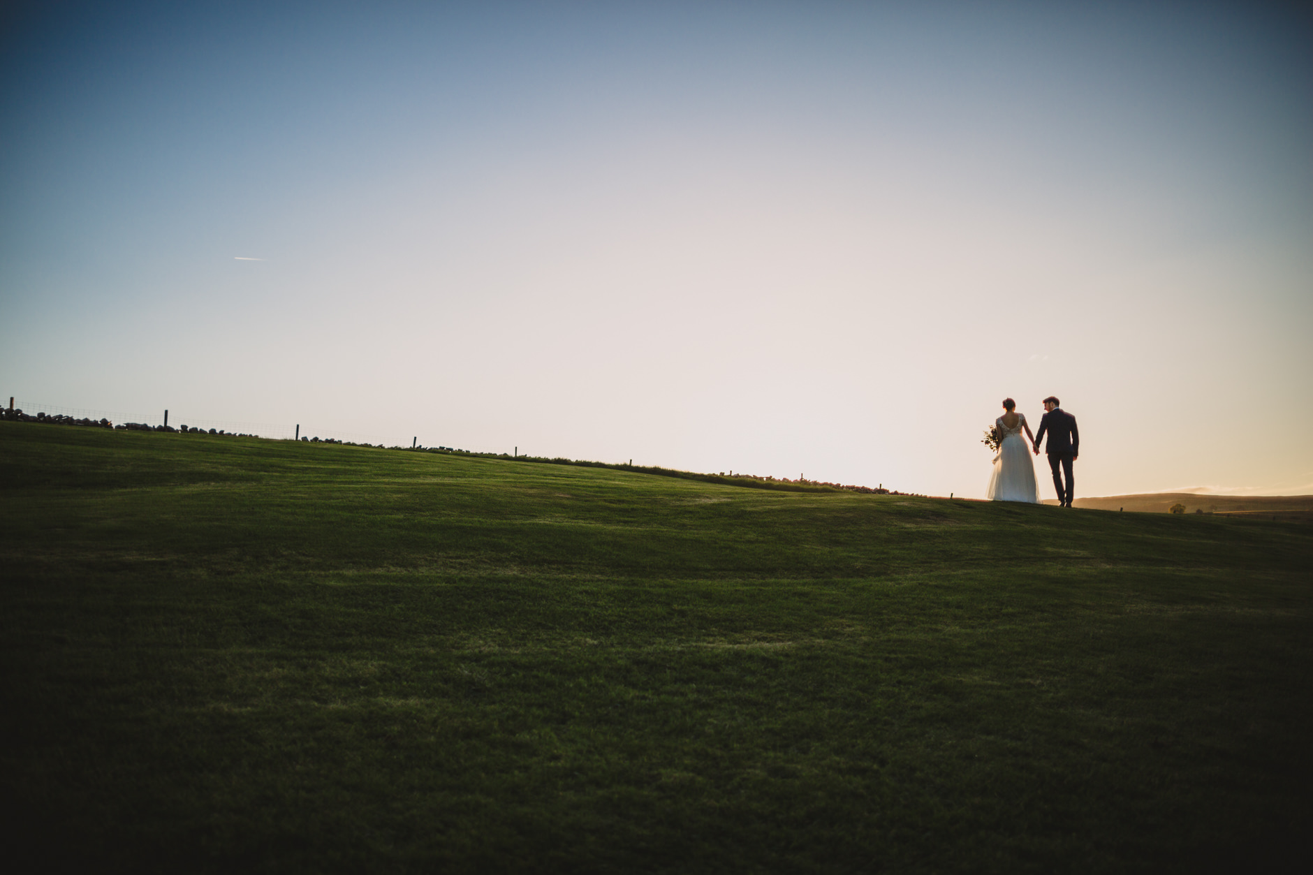 bride and groom strolling at sunset on the hill at knipe hall