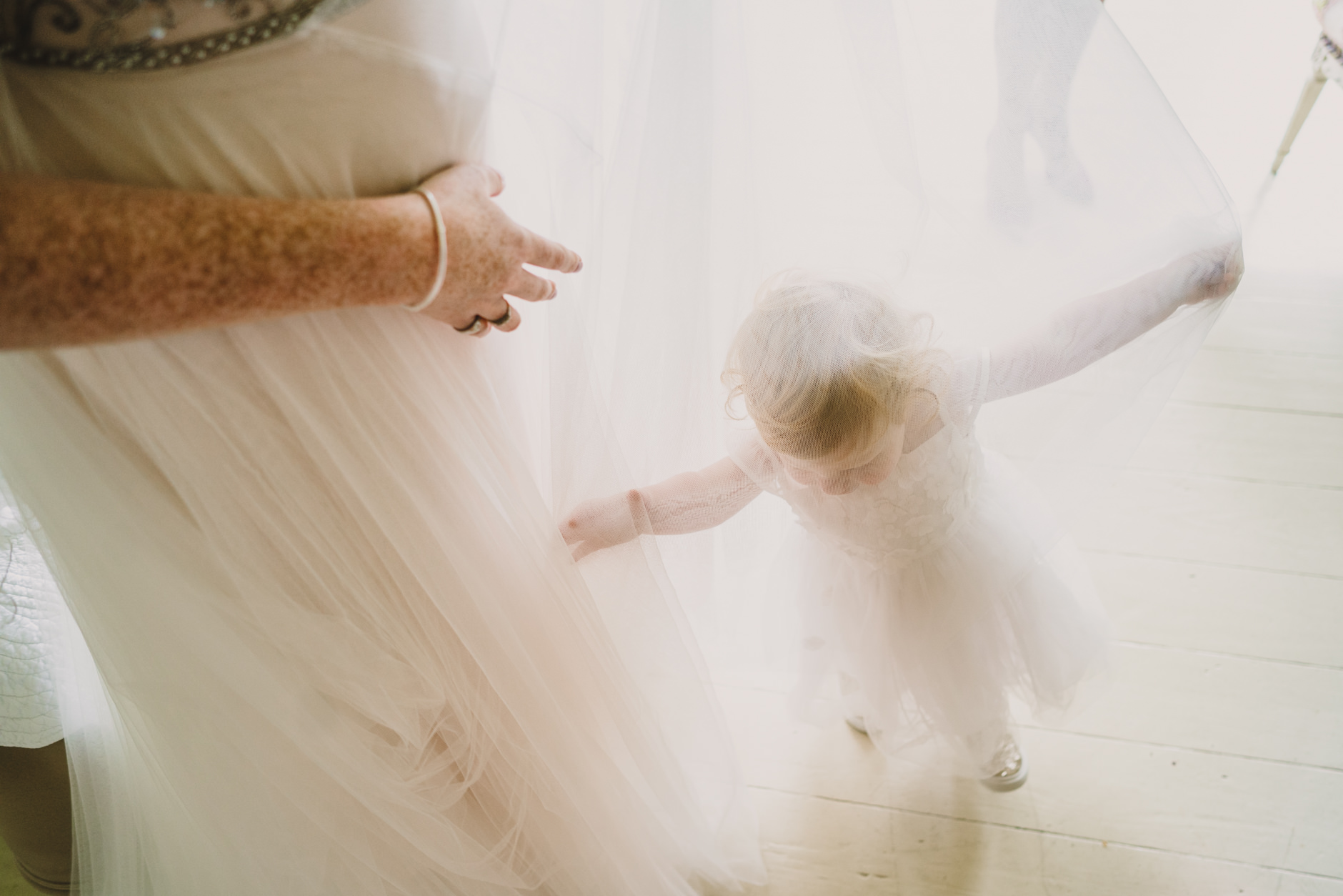 flower girl plays inside the layers of her mother's bohemian wedding dress