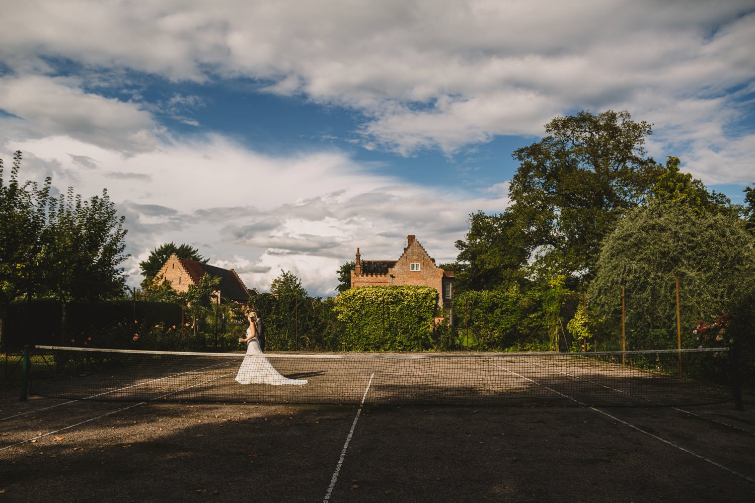 Bride and groom walking across tennis court Elms-Barn-Wedding-Norfolk